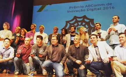 A imagem mostra um grupo de pessoas reunidas para um evento de premiação. A imagem representa a celebração dos vencedores do "Prêmio ABCOMM de Inovação Digital 2016", um evento que reconhece e premia iniciativas de inovação digital no setor de comércio eletrônico no Brasil.