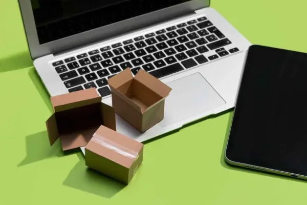 A imagem mostra uma laptop e um smartphone com pequenas caixas de entrega entre eles, simbolizando o comércio online e a logística. No contexto do artigo, isso reflete a escolha entre operar em um marketplace ou criar uma loja virtual, destacando a importância de considerar fatores como a infraestrutura de delivery, a experiência do cliente e a estratégia de marketing para determinar qual opção é mais adequada para o negócio em questão.