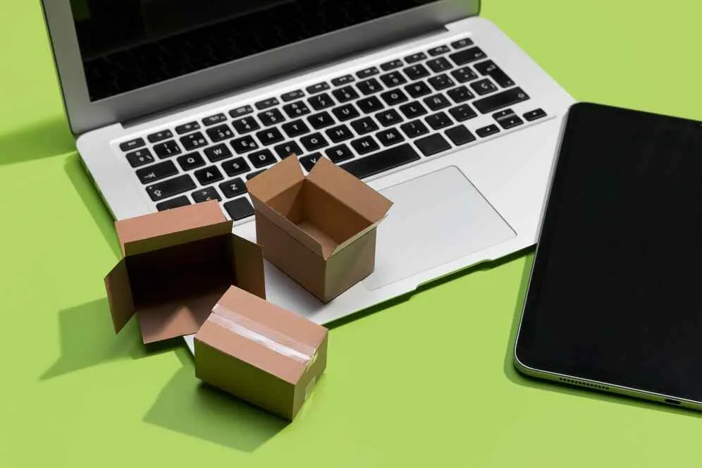 A imagem mostra uma laptop e um smartphone com pequenas caixas de entrega entre eles, simbolizando o comércio online e a logística. No contexto do artigo, isso reflete a escolha entre operar em um marketplace ou criar uma loja virtual, destacando a importância de considerar fatores como a infraestrutura de delivery, a experiência do cliente e a estratégia de marketing para determinar qual opção é mais adequada para o negócio em questão.
