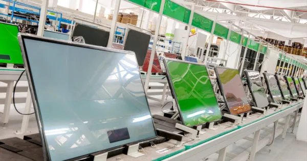 A imagem mostra uma linha de montagem de telas de televisão em uma fábrica, com várias telas em diferentes estágios de montagem e testes. As telas estão conectadas a cabos e dispositivos, o que sugerem uma operação de montagem e verificação de funcionamento. No contexto do artigo "Direct to Consumer (D2C) no e-commerce: por onde começar?", a imagem pode ser usada para ilustrar a importância da produção e do fornecimento na cadeia de valor do e-commerce. A linha de montagem simboliza a transformação de componentes em produtos finais, o que é um passo crucial para a implementação de um modelo de negócios D2C. Este modelo envolve a venda direta de produtos aos consumidores, removendo intermediários e potencialmente reduzindo custos. A imagem destaca a necessidade de uma cadeia de fornecimento eficiente e de um processo de montagem e distribuição bem-sucedido para o sucesso de uma estratégia D2C no e-commerce.