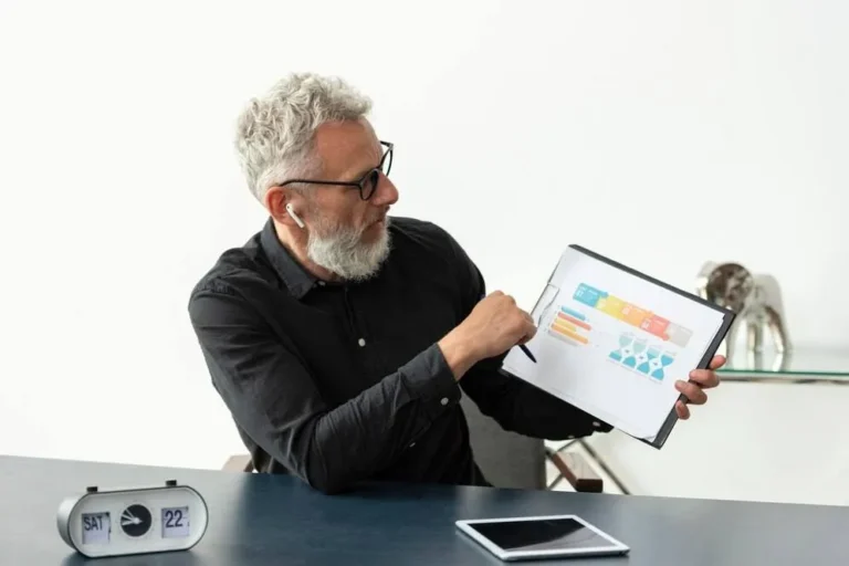 A imagem mostra um homem de negócios analisando um relatório com gráficos, simbolizando a importância da monitoração e do gerenciamento de KPIs (Indicadores de Desempenho Chave) na logística. No contexto do artigo, isso reflete a necessidade de acompanhar e otimizar indicadores-chave, como o tempo de entrega, a precisão da entrega, o custo da logística e a satisfação do cliente, para melhorar o desempenho e a eficiência das operações logísticas da empresa.