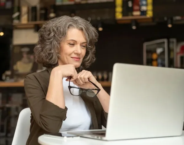 A imagem mostra uma mulher de negócios em um ambiente de trabalho, olhando para um notebook com um sorriso, simbolizando a satisfação e o sucesso no comércio online. No contexto do artigo sobre marketplaces de nicho, isso reflete a importância de se especializar em segmentos específicos do mercado para atingir clientes específicos e construir uma forte identidade de marca, o que pode levar a maior fidelidade do cliente e a uma posição mais competitiva no varejo digital.