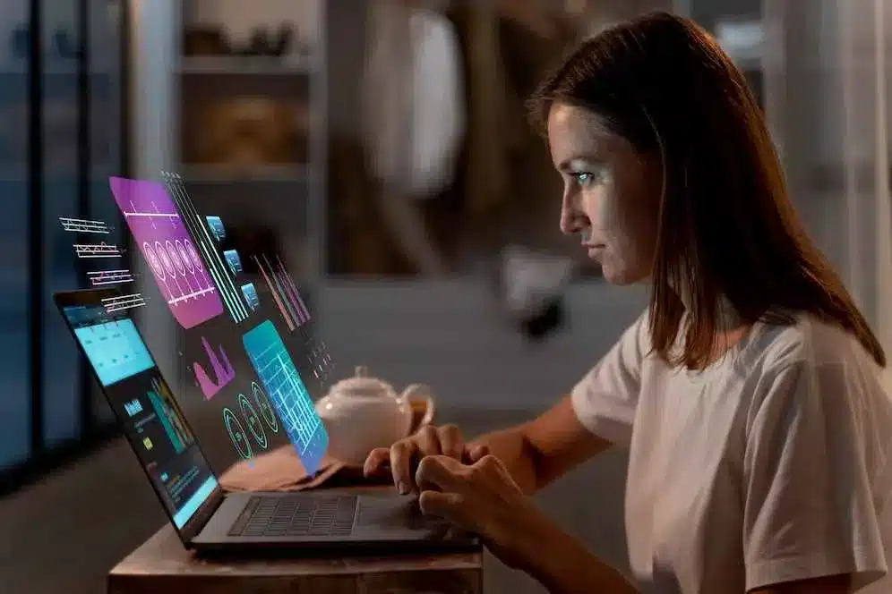 A imagem mostra uma mulher analisando gráficos e dados em um laptop, com ícones e indicadores de performance em volta, simbolizando a gestão e a análise de desempenho da operação. No contexto do artigo sobre inteligência operacional, isso reflete a importância de usar dados e análises para tomar decisões informadas, otimizar processos e, resultando em maior satisfação do cliente e melhor desempenho da empresa.