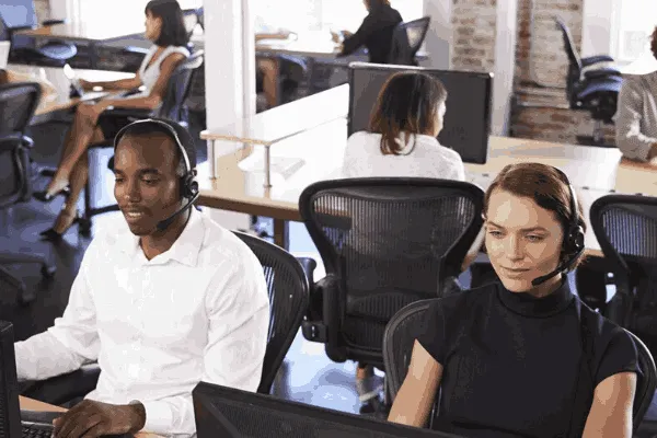 A imagem mostra um ambiente de escritório com várias pessoas usando fones de ouvido e interagindo com computadores. Um homem e uma mulher que estão sentados lado a lado, ambos com fones de ouvido e olhando para suas telas de computador. A mulher está falando em um microfone, enquanto o homem está digitando. No contexto do material "Combine relacionamento com o cliente e transformação digital!", a imagem pode ser usada para ilustrar a importância de um atendimento ao cliente eficaz e a integração de soluções digitais na gestão de relações com os clientes.
