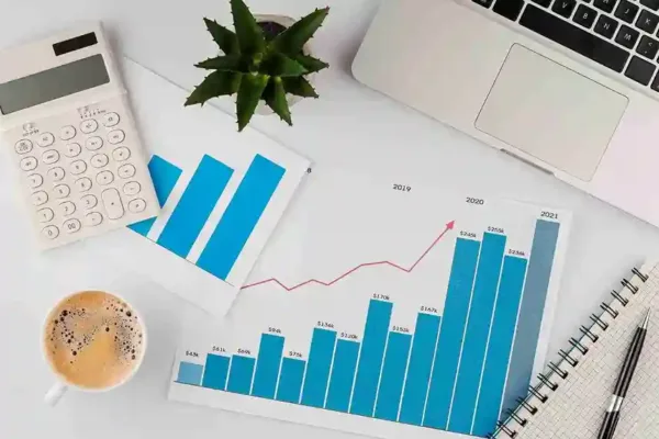 A imagem exibe um ambiente de trabalho com gráficos de crescimento, um notebook, um calculadora e um café, representando a análise de dados e o planejamento para aproveitar o crescimento do e-commerce. Indica a importância de monitorar métricas-chave, como vendas e receita, e a necessidade de estratégias baseadas em dados para capitalizar o boom do varejo online.