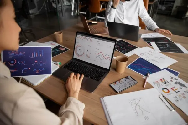 A imagem mostra uma reunião de negócios com colaboradores analisando gráficos e relatórios, simbolizando a gestão de informações e processos. No contexto do artigo sobre RPA (Automação de Robótica Processual), isso reflete como a implementação da RPA pode aumentar a produtividade, ao automatizar tarefas repetitivas e permitir que os funcionários se concentrem em atividades mais estratégicas e criativas, resultando em uma gestão mais eficiente das operações da empresa.