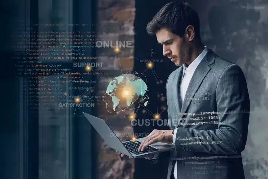 A imagem mostra um homem de terno segurando um laptop, com elementos gráficos e código de programação ao fundo, sugerindo um ambiente de tecnologia e negócios. Ilustra a importância do BI para a gestão da empresa, pois a integração de tecnologia e análise de dados pode fornecer insights valiosos, permitindo uma tomada de decisão mais embasada e melhorando a eficiência operacional.