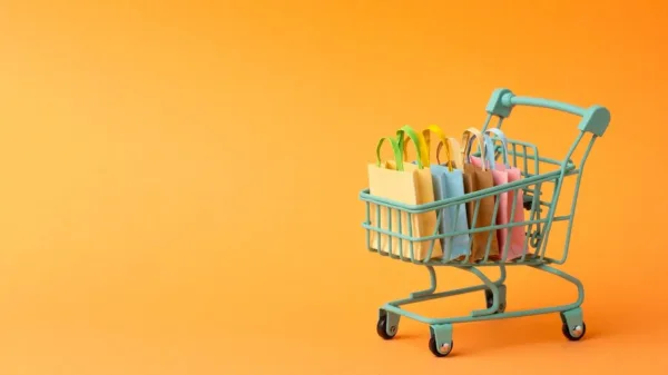 A imagem apresenta uma carrinha de compras colorida, cheia de sacolas de diferentes cores, em um fundo de cor laranja. A carrinha está em um estado de repouso, mas cheia de itens, o que pode simbolizar a quantidade de compras feitas. No contexto do artigo "Entenda como o brasileiro consome no varejo online", a imagem pode ser usada para ilustrar o comportamento de compra online no Brasil. A diversidade de sacolas pode representar a variedade de produtos comprados e a preferência dos consumidores por fazerem compras em diferentes lojas virtuais.
