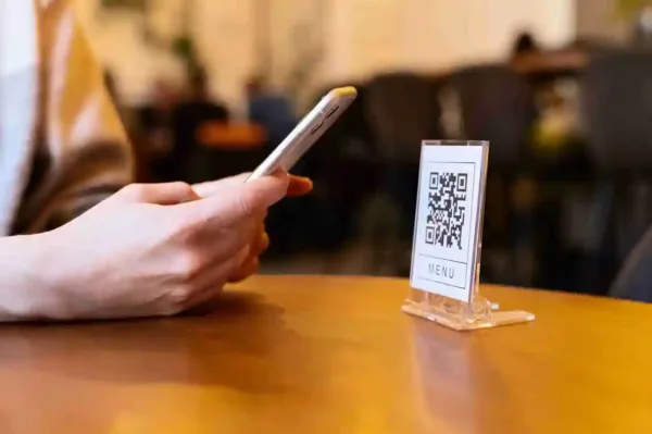 A imagem mostra uma pessoa digitalizando um QR code de menu em um estabelecimento, simbolizando a integração de tecnologias digitais em negócios. No contexto de um artigo sobre clubes de assinatura, isso pode indicar a facilidade de acesso a informações e a personalização de experiências para os clientes, além de oferecer benefícios como fidelidade e engajamento para os negócios que adotam esse modelo.