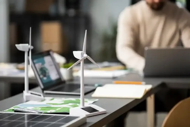 A imagem exibe um ambiente de trabalho com uma mesinha contendo uma solar panel (painel solar), dois modelos de eólicos (turbinas de vento), um tablet, um smartphone e um laptop. Esses elementos refletem a integração de tecnologias renováveis no dia a dia dos negócios, o que é relevante para o artigo sobre o "Impacto de ferramentas tecnológicas renováveis no negócio". A presença desses dispositivos e modelos sugere a exploração de fontes de energia limpa e a adoção de soluções sustentáveis, que podem reduzir custos, melhorar a eficiência energética e reforçar a imagem de responsabilidade ambiental da empresa.