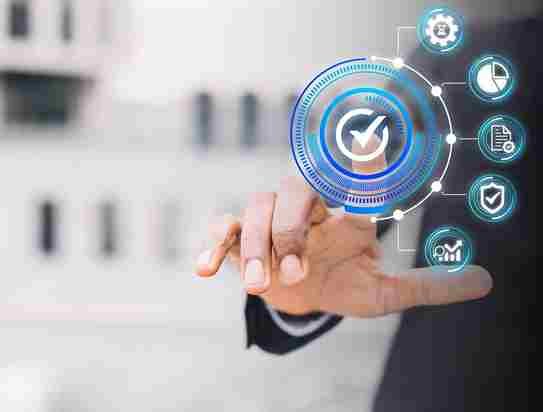 A imagem apresenta uma pessoa em um ambiente de escritório apontando para um gráfico de ciclo PDCA (Plan-Do-Check-Act), que é um modelo de gestão de qualidade e melhoria contínua. O ciclo é representado por ícones e setas que mostram a sequência do processo: planejar (Plan), executar (Do), verificar (Check) e agir (Act). O gráfico é visualizado como uma interface gráfica interativa, sugerindo a utilização de tecnologia para apoiar a implementação do ciclo PDCA.