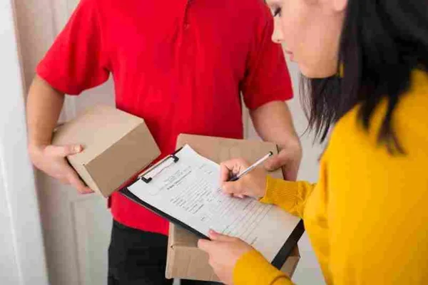 A imagem mostra uma pessoa vestida de vermelho segurando uma caixa e uma mulher de amarelo segurando uma prancheta e anotando algo. Isso sugere que o conteúdo está relacionado a processos de troca e devolução de produtos, provavelmente no contexto de comércio eletrônico ou varejo. A imagem parece estar associada a um artigo que aborda estratégias e melhores práticas para evitar problemas e minimizar os custos relacionados a trocas e devoluções de produtos, visando melhorar a experiência do cliente e a eficiência operacional da empresa.