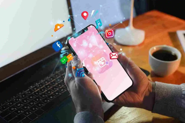 A imagem mostra uma mão segurando um smartphone com diversos ícones de redes sociais e aplicativos flutuando ao redor. Isso sugere que o conteúdo está relacionado a tendências e estratégias de social commerce, ou seja, a integração do comércio eletrônico com as redes sociais.