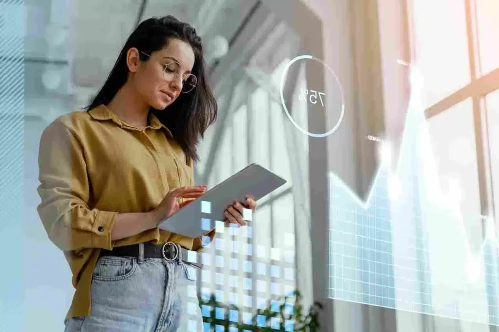 A imagem mostra uma mulher segurando um tablet e interagindo com uma interface digital projetada em uma parede. Isso sugere que o conteúdo está relacionado a sistemas de planejamento de recursos empresariais (ERP) e suas diferentes modalidades. A imagem parece estar associada a um artigo que apresenta e descreve os principais tipos de sistemas ERP disponíveis no mercado, destacando suas características, funcionalidades e aplicações no contexto empresarial.