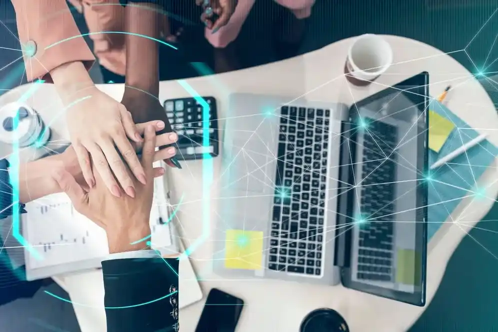 A imagem representa um cenário de trabalho em que várias pessoas estão envolvidas em atividades de gerenciamento e análise de dados, o que é relevante para o contexto de implementação de um Sistema ERP (Enterprise Resource Planning) no varejo. As mãos de um indivíduo estão apontando para um gráfico digital, que pode simbolizar a monitoração de KPIs (Indicadores Chave de Desempenho) essenciais para avaliar o sucesso pós-implementação de um ERP.