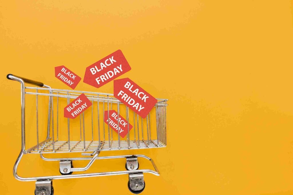 A imagem destaca a Black Friday, mostrando um carrinho de compras com tags que dizem "Black Friday", contra um fundo amarelo. Representa as grandes promoções e descontos que os consumidores esperam durante essa temporada de compras, que é um evento comercial importante para varejistas e compradores, oferecendo oportunidades de ganhos para ambas as partes.