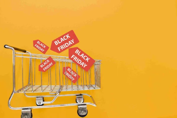A imagem destaca a Black Friday, mostrando um carrinho de compras com tags que dizem "Black Friday", contra um fundo amarelo. Representa as grandes promoções e descontos que os consumidores esperam durante essa temporada de compras, que é um evento comercial importante para varejistas e compradores, oferecendo oportunidades de ganhos para ambas as partes.