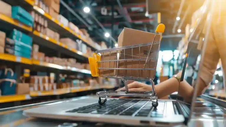 Carrinho de compras de metal em miniatura com pequenas caixas de papelão em cima do teclado de um notebook aberto. Ao fundo, um estoque organizado com prateleiras repletas de produtos. A imagem simboliza a integração de um sistema ERP com a plataforma Loja Integrada para automação de vendas, controle de inventário e gestão logística eficiente.